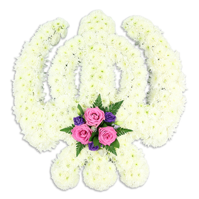 A reverent and visually striking Khanda floral tribute is centred in the frame, set before a smooth white background that allows its detailed construction to shine. The symbol of Sikhism is fully realised in flowers: the upright double-edged sword, the embracing circle of the chakkar, and the two curved kirpans sweeping down and out at the base are all covered in compact white chrysanthemum blooms. Each head is positioned to follow the natural line of the design, so the floral surface feels both structured and soft at once. From a distance, the arrangement appears almost sculptural, but up close the fine, feathery petals and gentle gradations of white to soft cream come into focus, creating a sense of quiet depth. Light falls evenly across the tribute, bathing it in a gentle luminosity, while a faint shadow under the bottom curve of the symbol hints at its three-dimensional form. At the lower centre, where the two kirpans cross, a contrasting cluster of flowers adds a note of tenderness. Three rich pink roses, perfectly fresh, are tucked in together, their petals curling delicately at the edges. They are accompanied by smaller, deep purple blooms and ferny green foliage that fans out just enough to frame the roses without overwhelming them. This accent feels like a heart cradled within the strength of the Khanda's blades, suggesting both protection and love. Such a tribute would be especially fitting for Sikh funerals, cremation services, or memorials in the Emerson Park and Hornchurch area, where families often look for meaningful floral designs. It has the quiet confidence of a piece made by local experts who understand both the spiritual symbolism and the emotional weight these flowers will carry on the day.