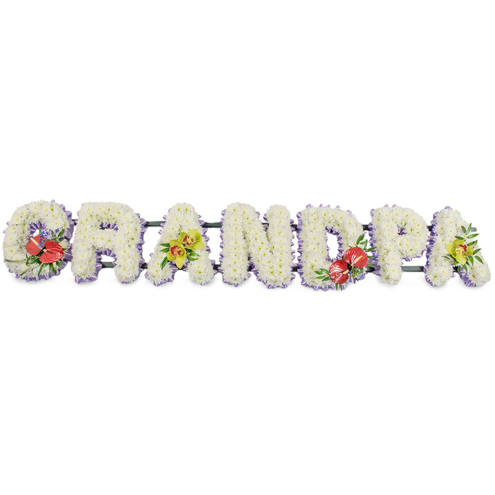 This image presents a traditional letter tribute spelling GRANDPA in large, solid block capitals, arranged in a straight line against a clean white studio background so that the flowers stand out with clarity. Each letter is completely filled with tightly packed white chrysanthemums or similar small blooms, their rounded forms and layered petals creating a richly textured, cushion-like effect that reads as peaceful and comforting from a distance. The consistent white colour gives the piece a serene, almost luminous quality, suitable for a funeral or memorial service. Around the base of each letter, a narrow edging of soft lavender ribbon provides a delicate border, lending subtle colour contrast and helping to define the shapes without detracting from the tranquillity of the white flowers. Behind the letters, dark green bars and stems provide structural support, keeping the entire tribute strong and aligned while remaining mostly hidden from view. Carefully positioned accent arrangements bring depth and storytelling to the design. On the G and the D, bold clusters of deep red anthuriums stand proud, their glossy, heart-shaped spathes and bright central spadices nestled amongst lush green foliage and specks of tiny purple filler flowers. These rich tones suggest enduring love, respect, and cherished memories. On the first A and the final A, arched sprays of yellow-green orchids introduce a fresh, graceful note, their slender petals and lime hues hinting at hope and the continuity of family ties. This personalised GRANDPA flowers tribute would feel at home in a quiet Emerson Park chapel or at a crematorium service near Hornchurch, a lovingly crafted display that allows relatives to express their affection and farewell through carefully chosen funeral flowers.